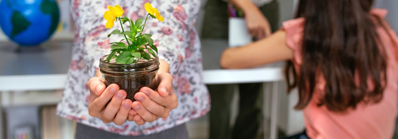 Female student showing to camera a pansy plant in ecology classroom