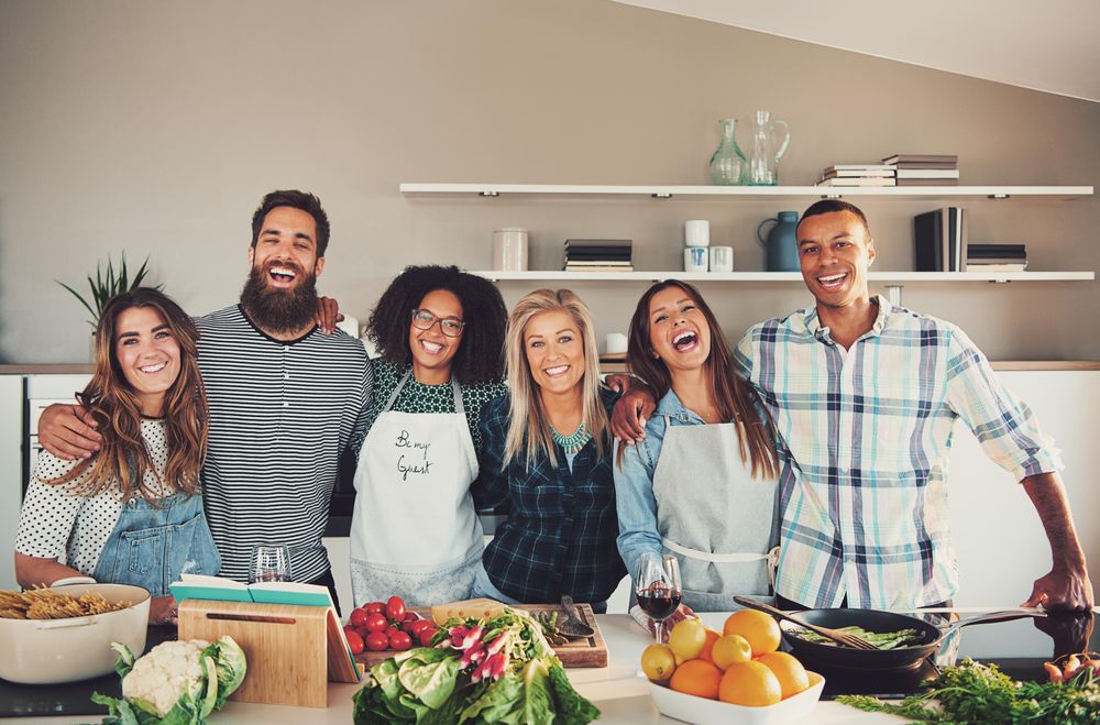 Happy friends posing for the camera while cooking together in the kitchen