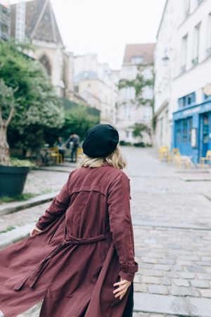 Woman in red coat with dark hat walking near residential building in Paris, France