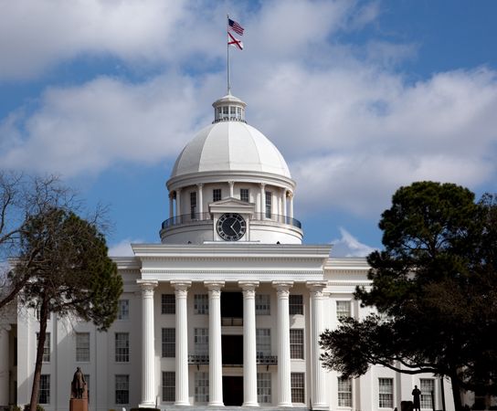 Front view of majestic stone Alabama State Capitol building with flags in Montgomery