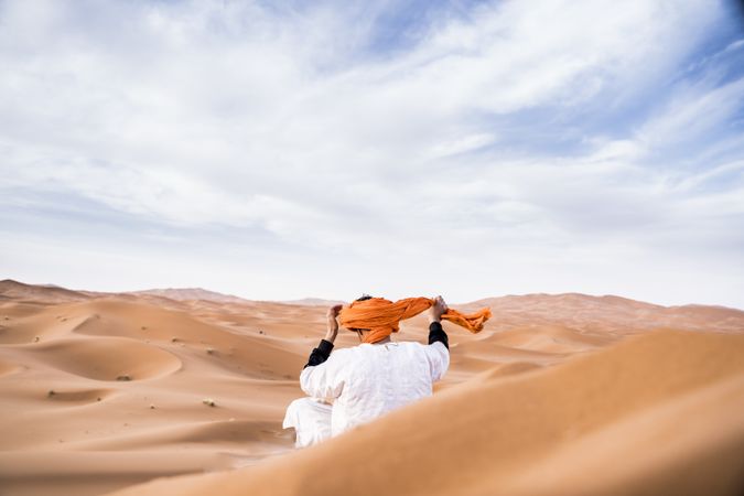 Man in turban sitting among sand dunes