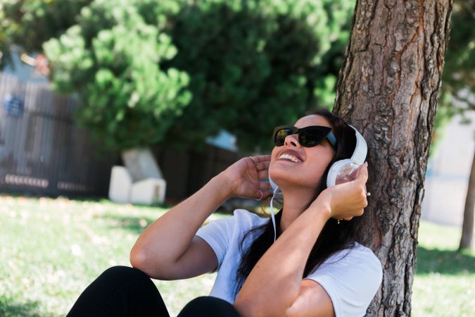 Relaxed trendy woman in headphones resting in park on grass