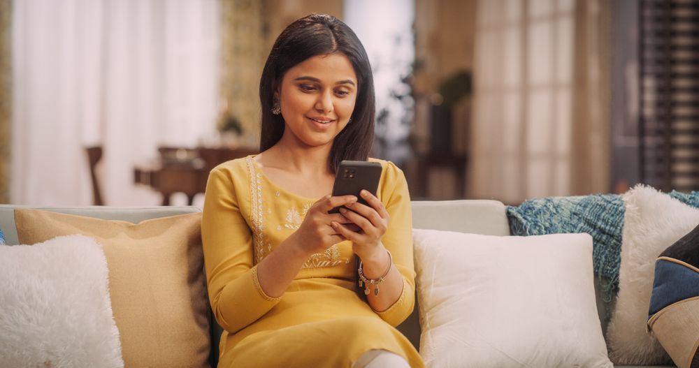 Indian Female Using Smartphone Sitting on a Couch in Cozy Home