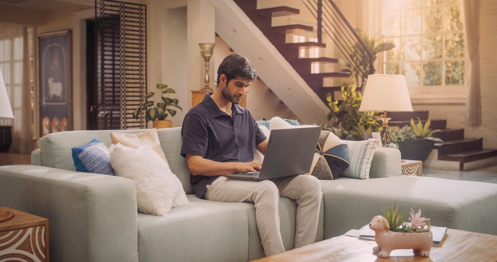 Focused Hindu Man Typing on Laptop, Engaging in Remote Work in Cozy Home Office, Completing e-Commerce tasks