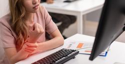 Asian woman holding her painful wrist while sitting at her desk
