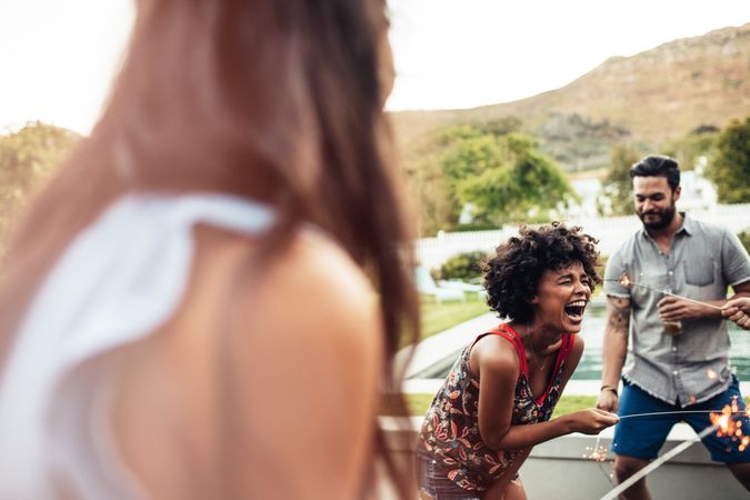 Young woman laughing with friends in backyard celebrating with sparklers