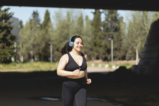 A strong young woman plays sports and runs in the park happy, listening to music with headphones