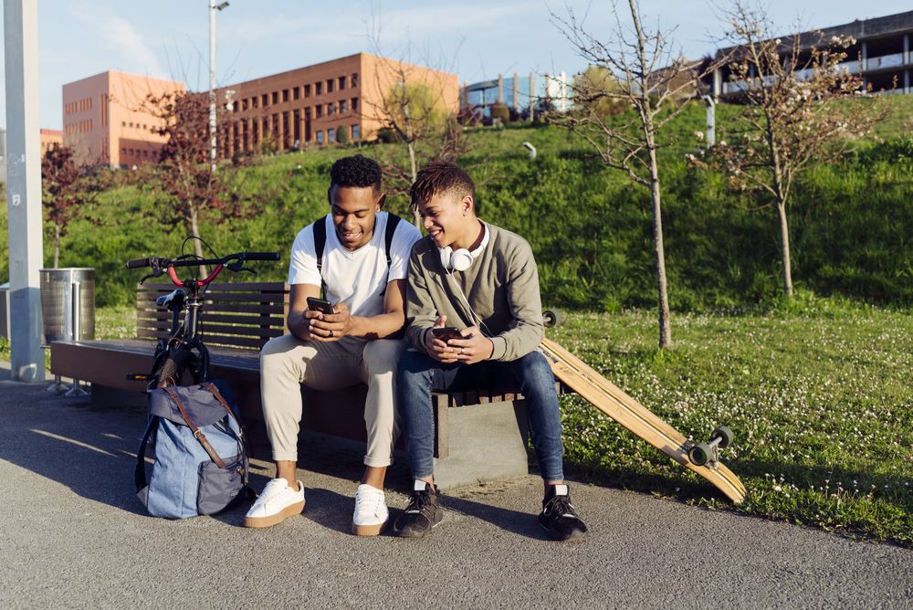 Young Black men sitting on bench with smartphone
