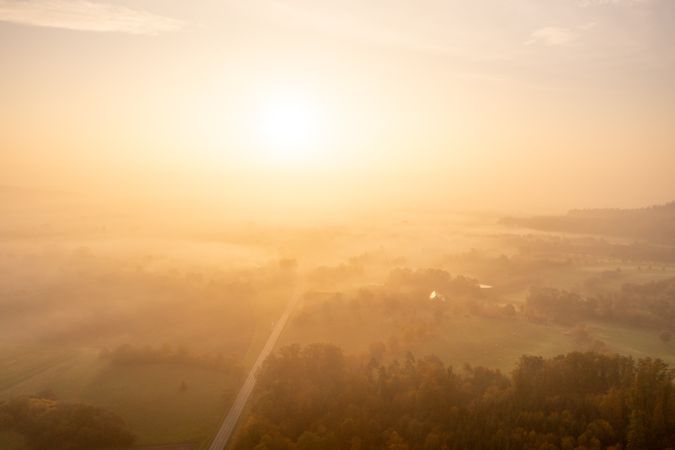 Drone image on a foggy morning of autumn at sunrise with multicolored trees and road