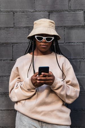 Black woman using smartphone near brick wall