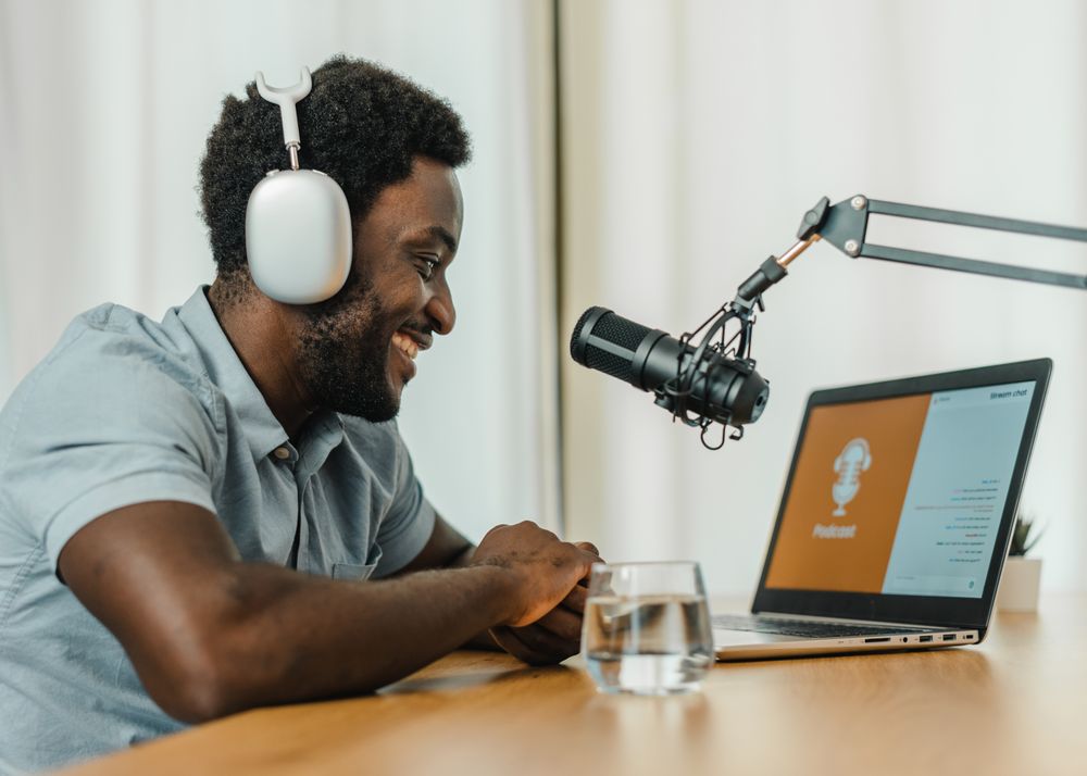 Smiling Black man using laptop and recording podcast