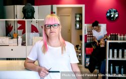 Hairdresser with pink hair in salon with client having hair washed in background 5QJ9G4