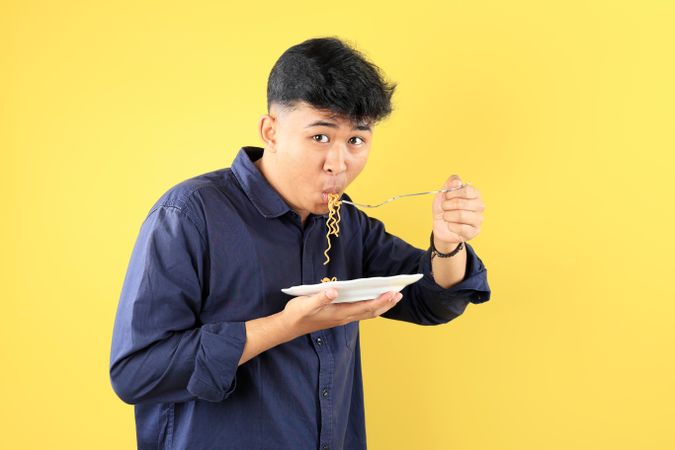 Indonesian Young Student Eating Instant Noodle using Stainless Fork.
