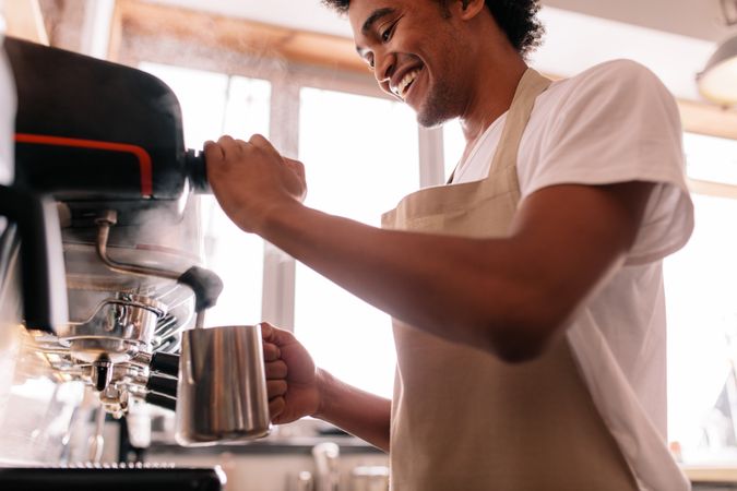 Happy young man preparing coffee at counter