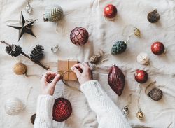 Flat-lay of holiday decoration, with hands tying box, top view