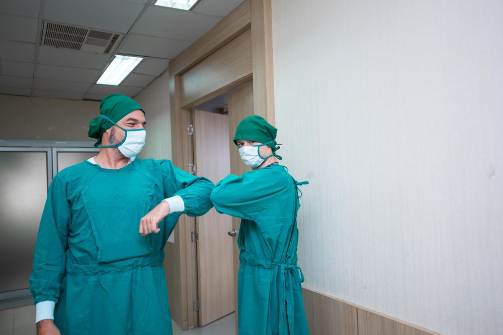 Two medical professionals in scrubs greeting each other with elbow bump in hallway