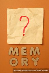 The word “Memory” written in cork below post it note on dusty orange background, vertical 5l8ZM5