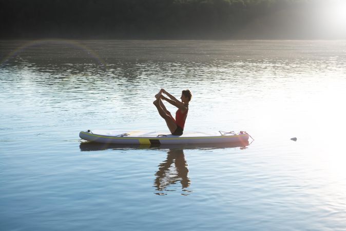 Woman doing leg stretch on paddleboard in the sunrise