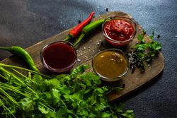 Three traditional Georgian condiments tomato satsebeli, yellow and red tkemali with ingredients on wooden board