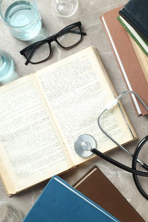Books, stethoscope, glasses and flasks on gray background, top view