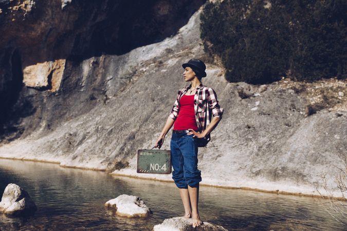 woman standing on rock with case near clear water in lake