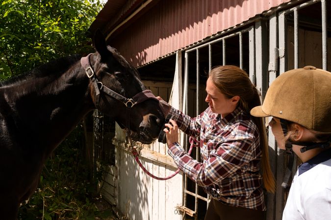 Woman and child together grooming horse outside