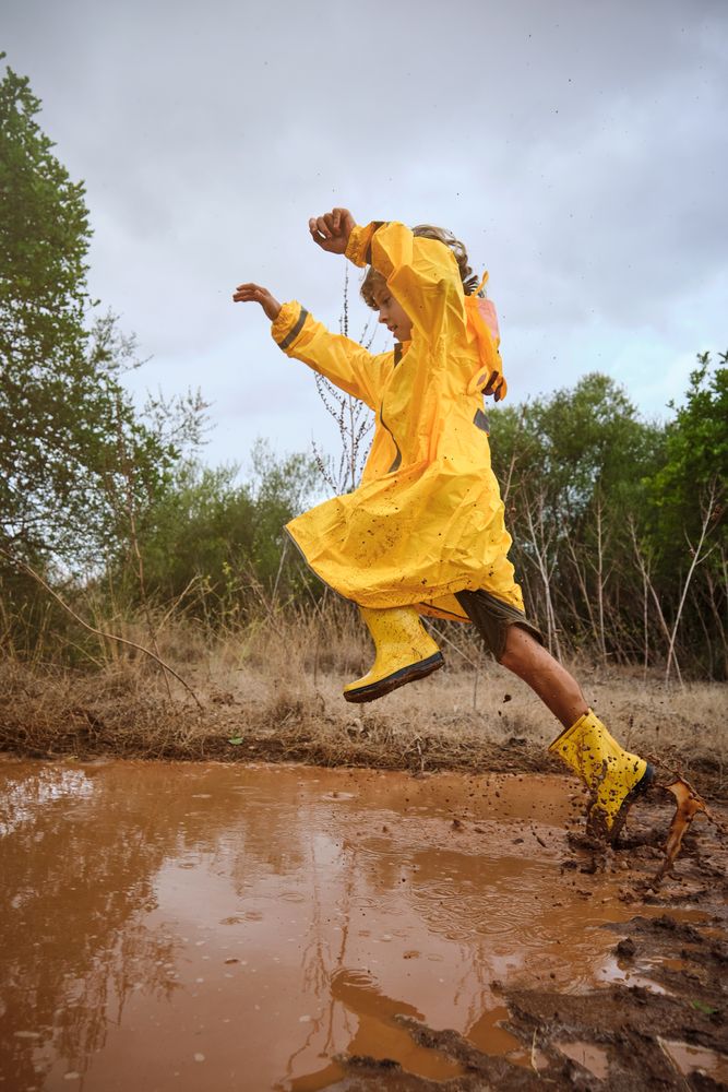 Preteen boy jumping over puddle