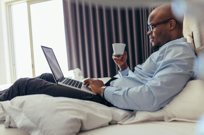 Man in office clothes working on laptop while lying in bed