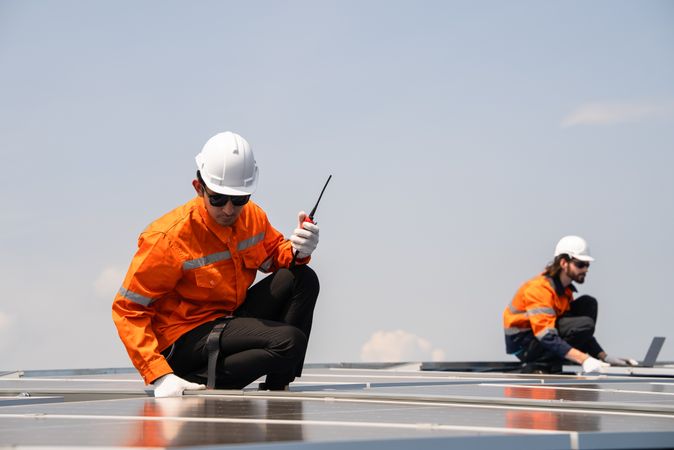 Male engineer checking solar cell  or photovoltaic cell by electronic device installed on the roof of the factory. Technician worker repair or inspect the system. Industrial renewable energy concept