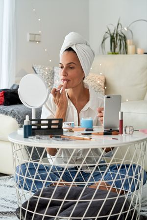 Woman applying makeup at home with mirror