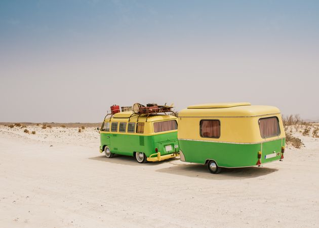 Colorful minibus with trailer parked on sandy shore in sunny day