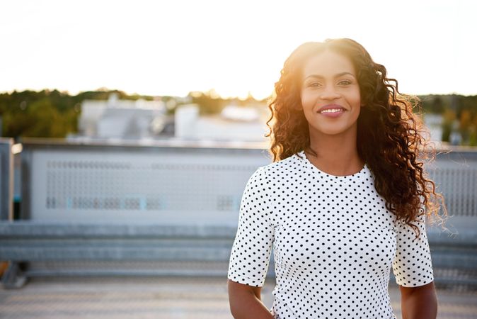 Relaxed happy Black woman on roof top with sun setting behind her