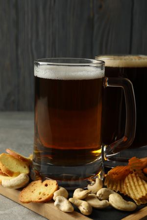 Beer and snacks on gray table against wooden background