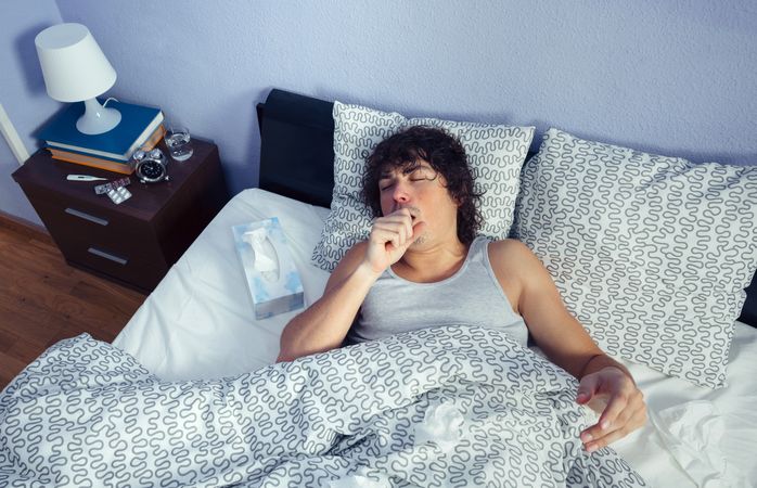 Portrait of sick man coughing lying in bed