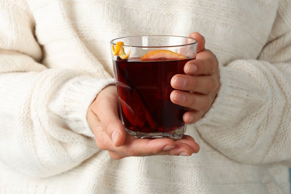 Girl in sweater holding glass with mulled wine, close up