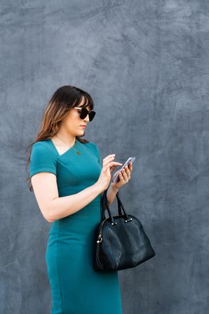Female in blue dress, sunglasses and handbag checking phone