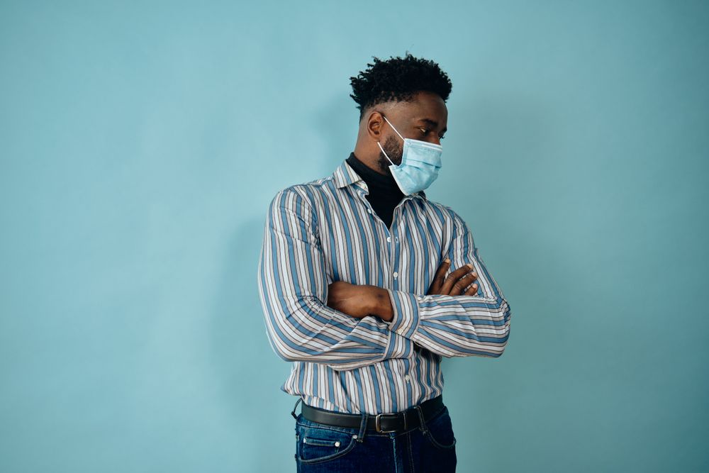 Portrait of a Black man in face mask blue striped shirt with his arms crossed looking away