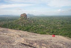 Tourist against solitary rock in middle of green forested plain under clear sky in summer