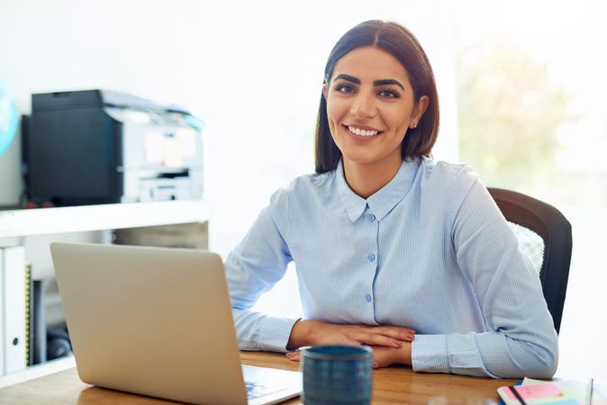Happy woman looking at camera from behind her laptop