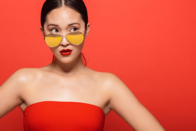 Stylish female model wearing sunglasses in red studio