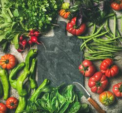 Fresh vegetables arranged with dark cutting board in center, square crop