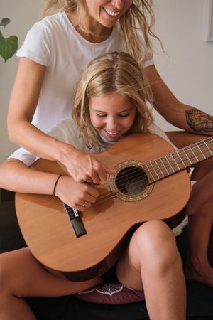 Blonde girl playing guitar while smiling with a woman sitting with her