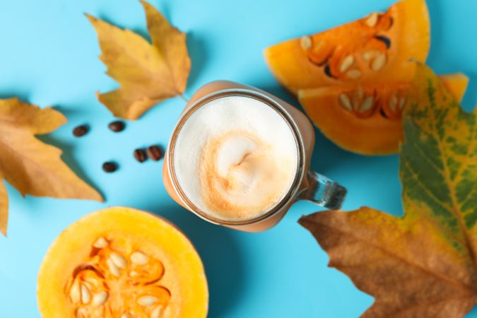 Composition with glass jar of pumpkin latte on blue background