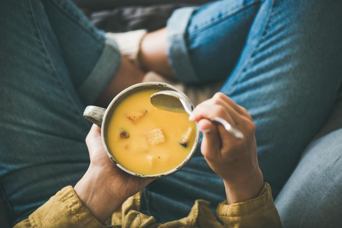 Woman in jeans holding spoon with cup of squash soup