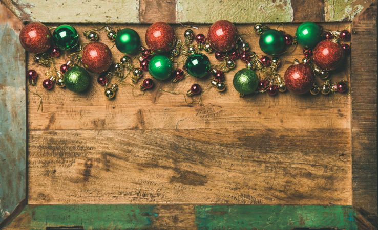 Tree ornaments on wooden board, large and small red, green and gold baubles, copy space