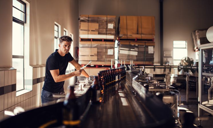 Young brewery business owner checking quality of beer bottles