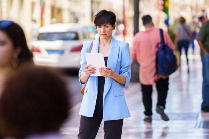 Woman in glasses and blue blazer standing on street with digital tablet