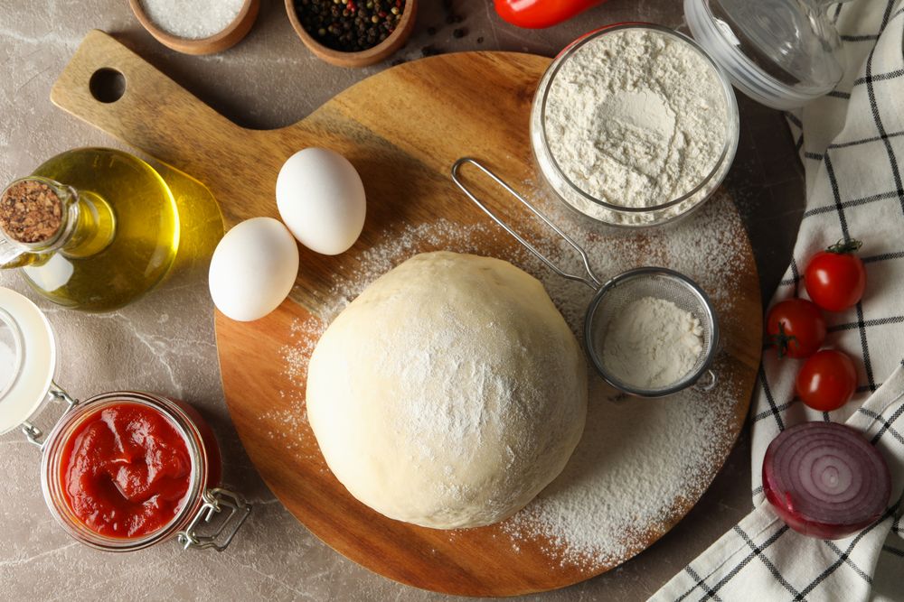 Dough and ingredients for cooking pizza on gray background