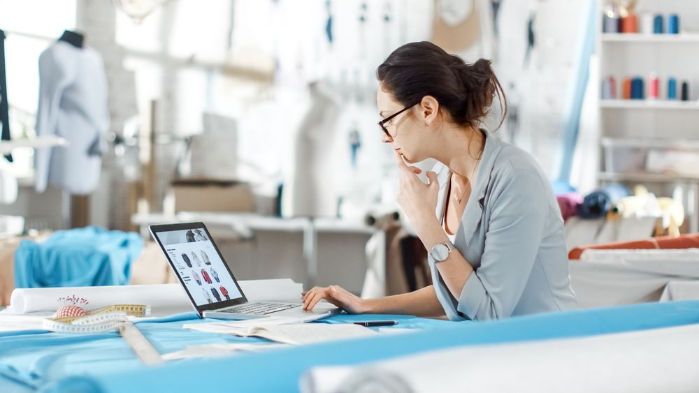 Woman fashion, designer,  Sitting at Her Desk Looking at Sketches on a Laptop