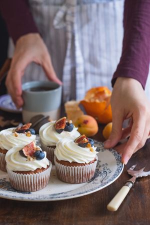 Person serving fresh baked carrot cupcakes decorated with frosting and fruit